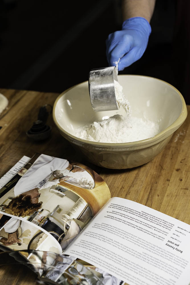 photo of a strawberry rhubarb pie hand pouring ingredients into bowl and cook book